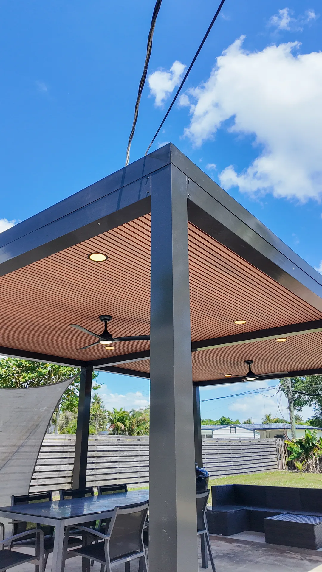 Custom aluminum pergola with wood-slat ceiling over a furnished Miami outdoor dining and lounge patio