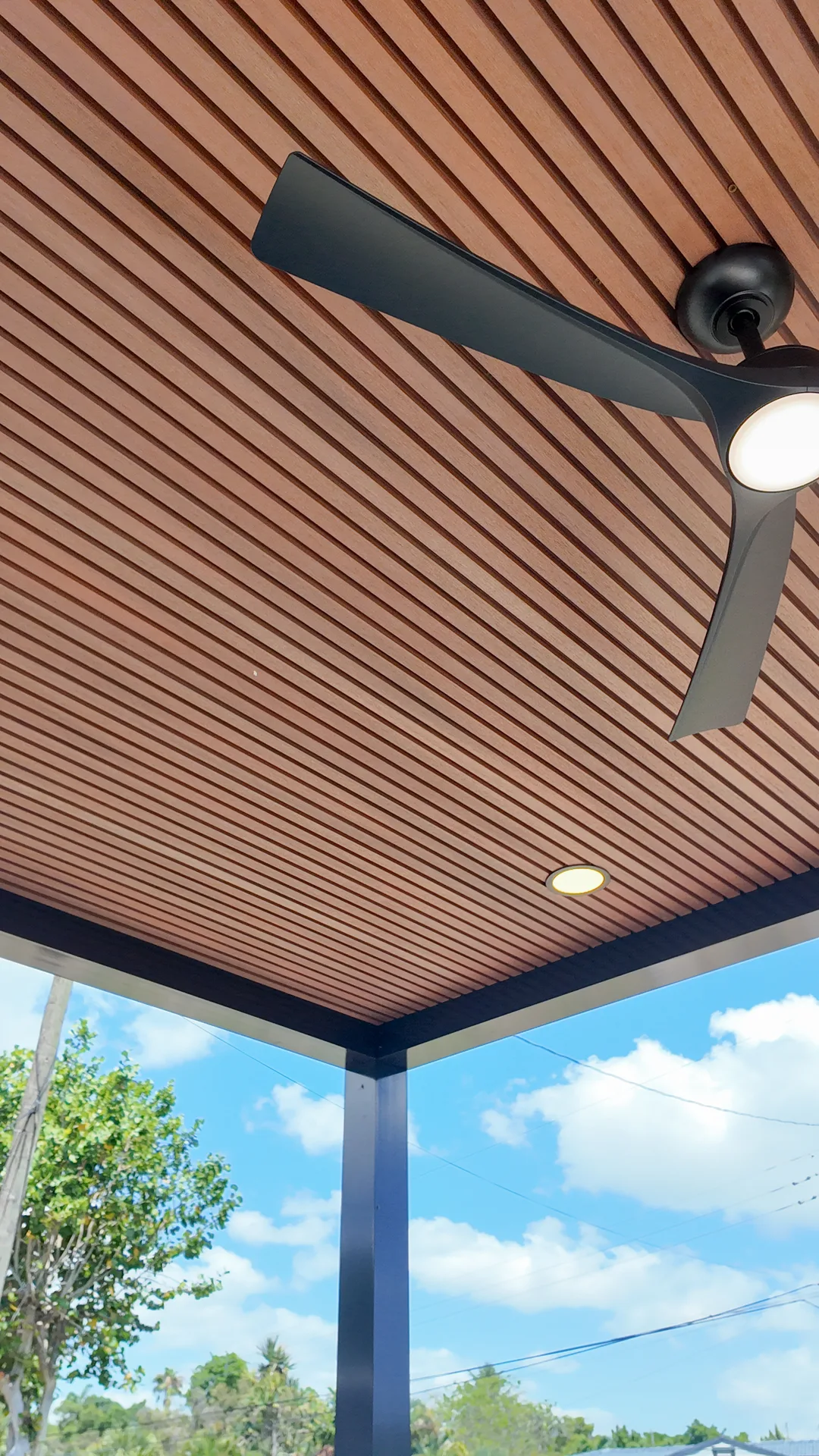 Close-up of a pergola wood-slat ceiling with a modern black fan and recessed lighting in Miami