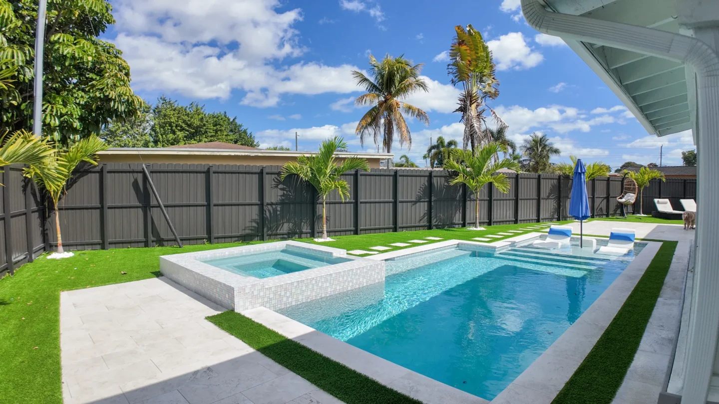 Modern pool and spa with glass-mosaic waterline tile in a Miami backyard by MIA Remodeling