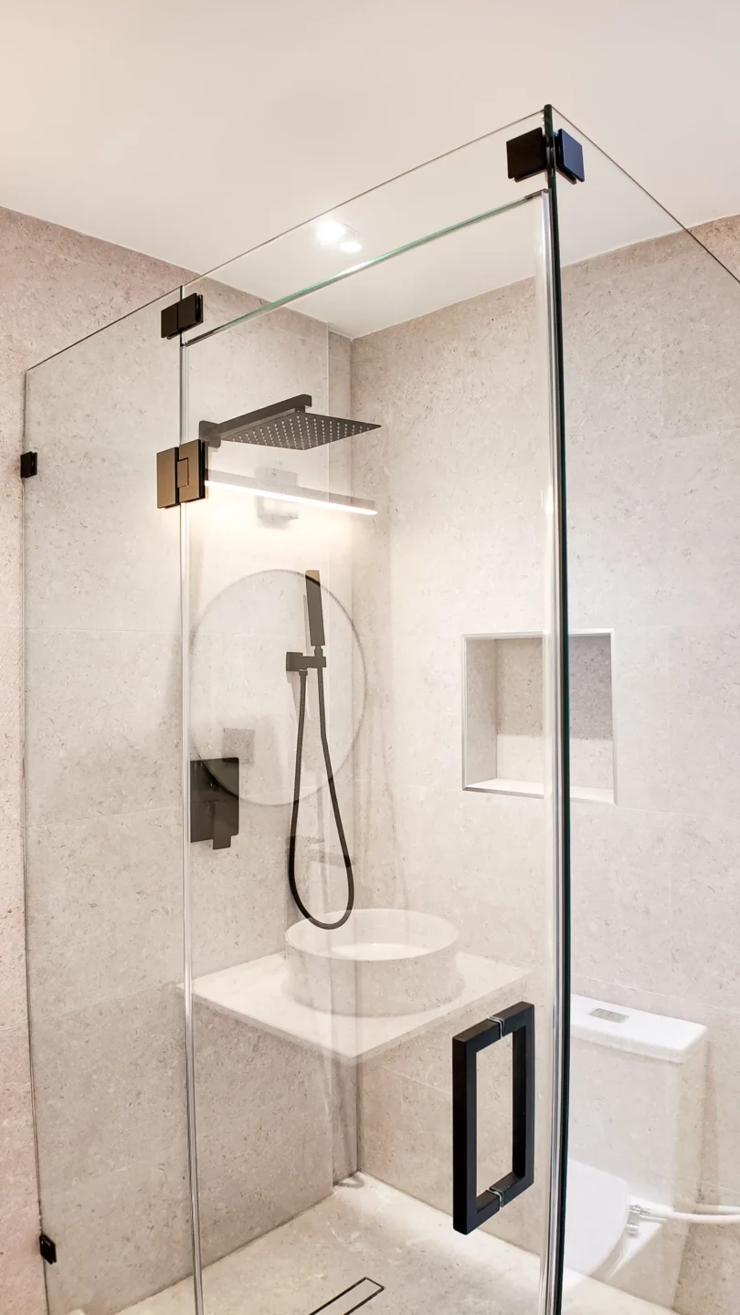 Frameless glass walk-in shower with marble-look walls and a built-in bench in an Aventura bathroom