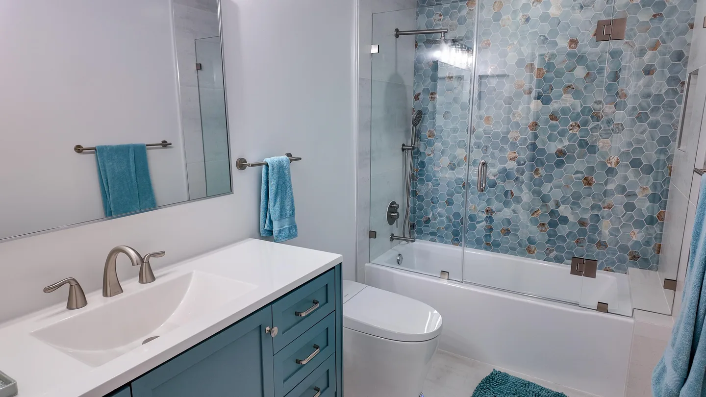 Bathroom with a white vanity beside a blue-tile bathtub and shower