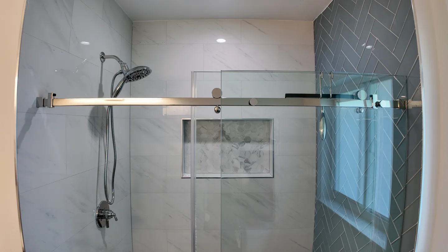 Walk-in shower finished in blue herringbone tile with a glass panel