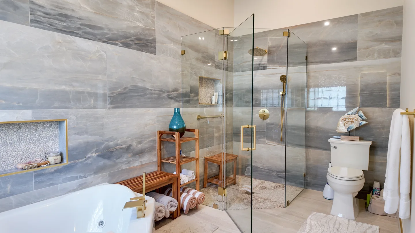 Frameless glass shower enclosure beside a soaking tub in a marble-look South Florida bathroom