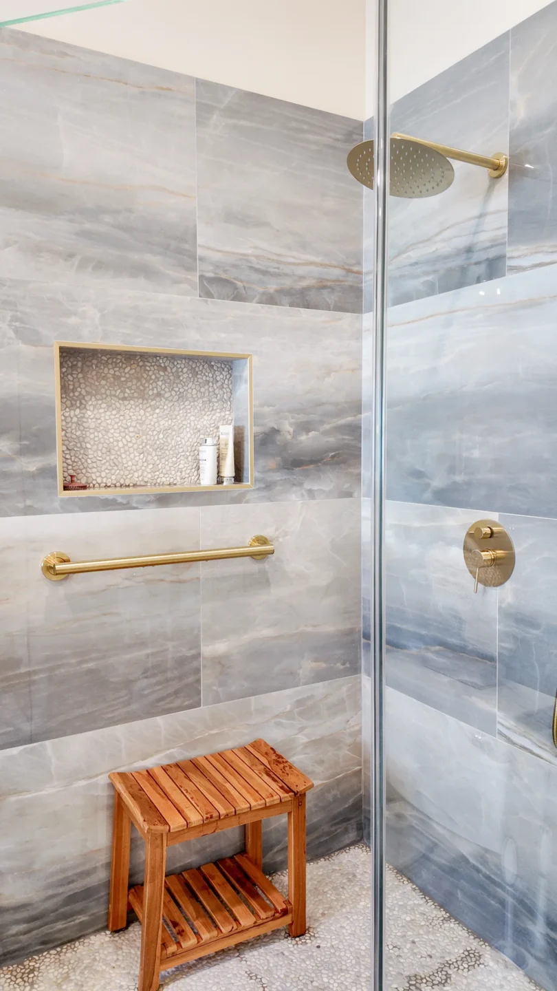 Frameless shower glass panel and door with brushed-brass fixtures and a teak bench