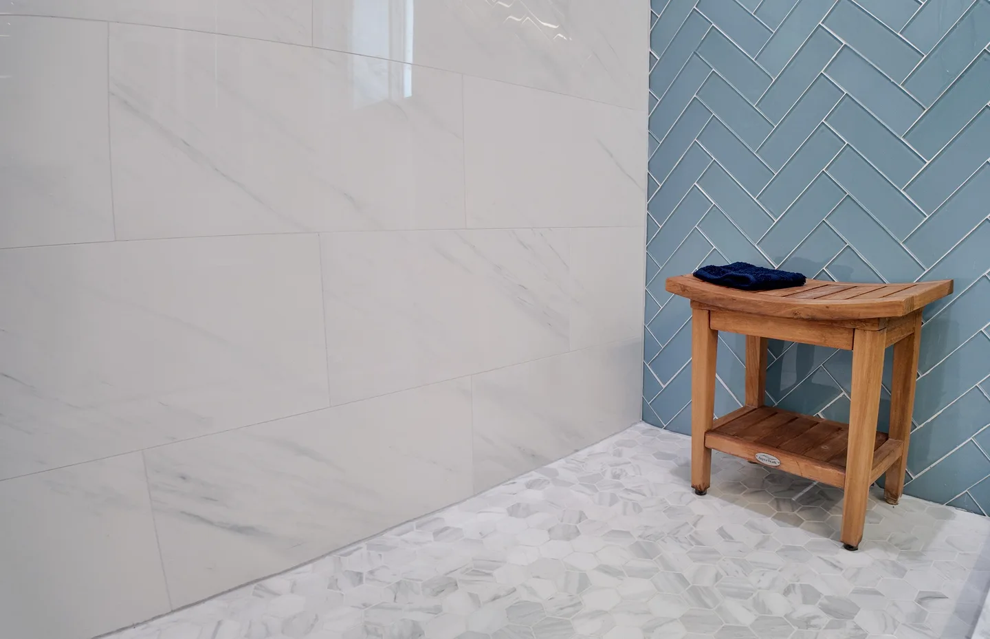 Blue herringbone shower tile with a teak bench and marble base