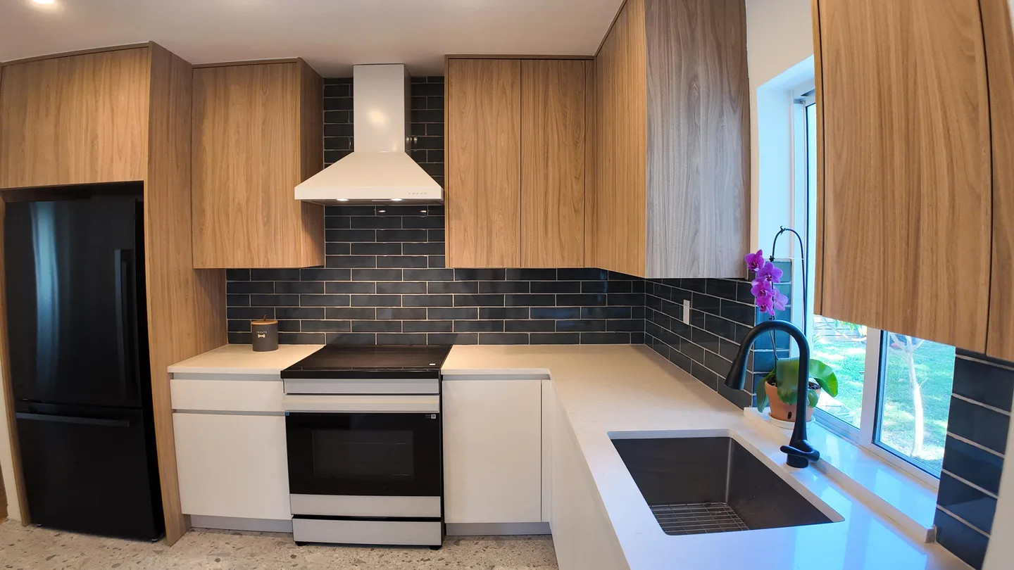 Kitchen with wood upper cabinets, white base cabinets, a range hood and subway backsplash