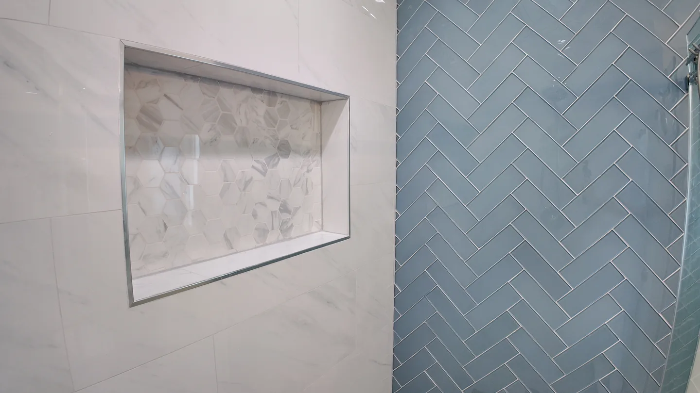 Recessed shower niche framed by herringbone tile and marble trim