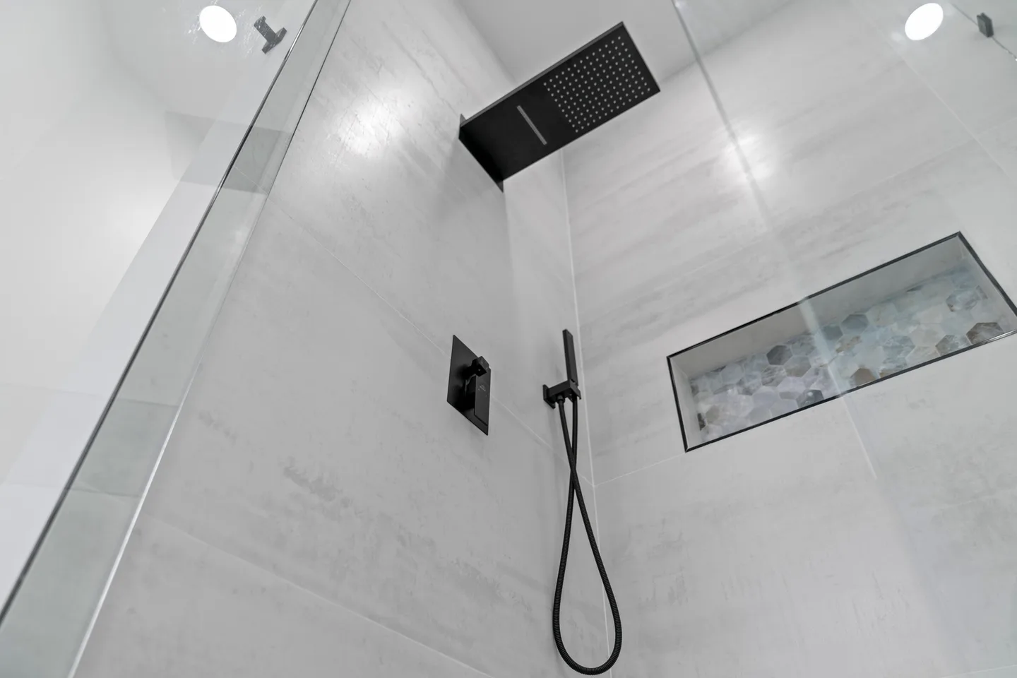 Tiled walk-in shower interior with a recessed niche and a rainfall showerhead